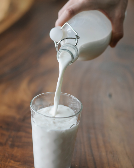 A clear glass filled with creamy raw milk on a wooden table, highlighting its natural, unprocessed appearance.