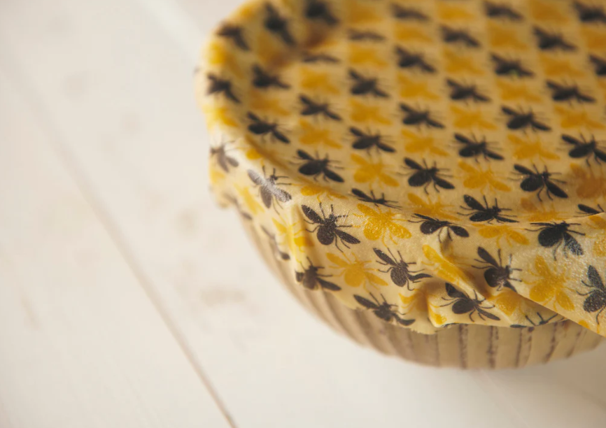 Beeswax food wrap covering a bowl on a light-colored table, sealed using the warmth of hands.