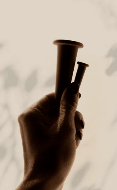 Hand gently holding translucent facial cupping tools casting soft shadows on a neutral background.