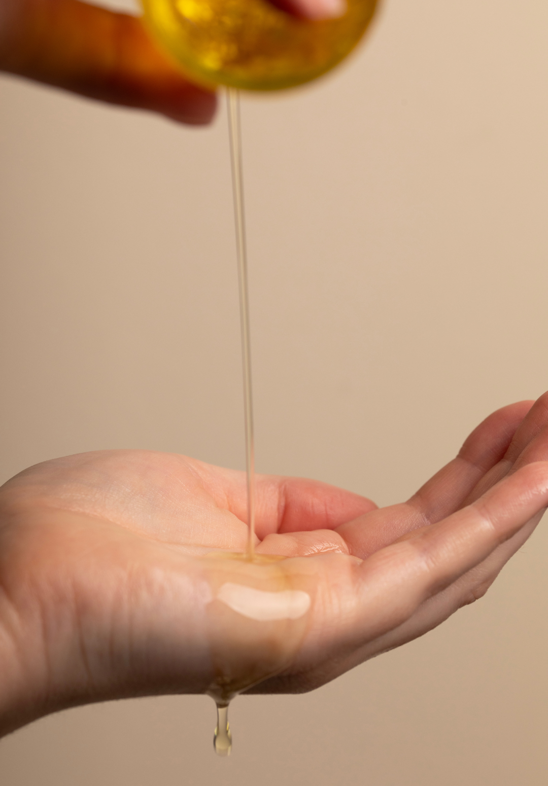 A close-up of a hand with baby oil being gently poured into the palm from a clear glass bottle