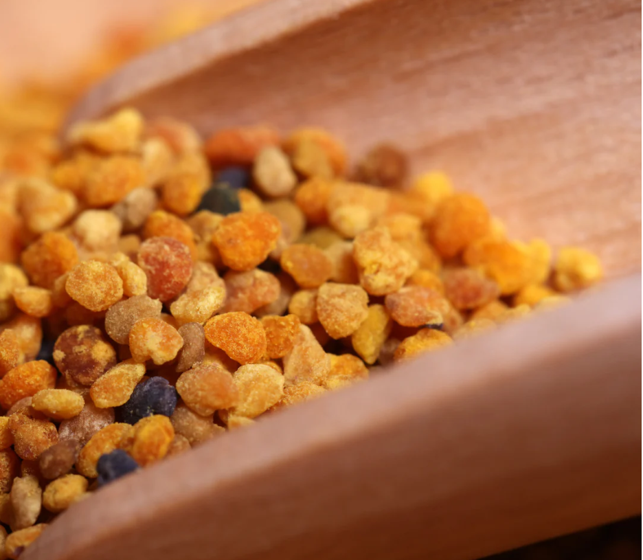 Wildflower bee pollen granules on a wooden spoon, showcasing their vibrant golden colour and natural texture.