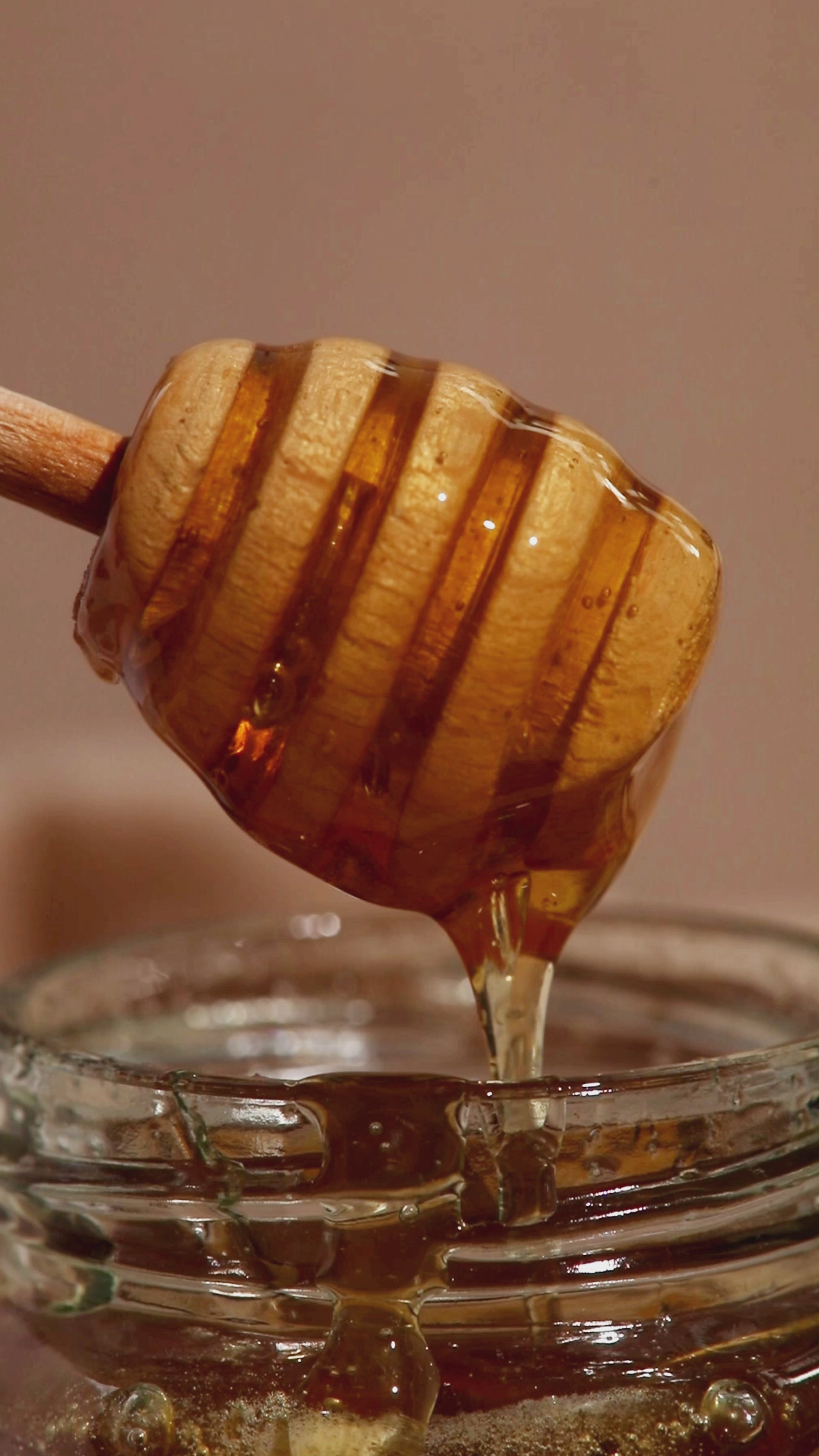 Golden raw wildflower honey dripping from a wooden dripper, highlighting its smooth texture and natural purity.