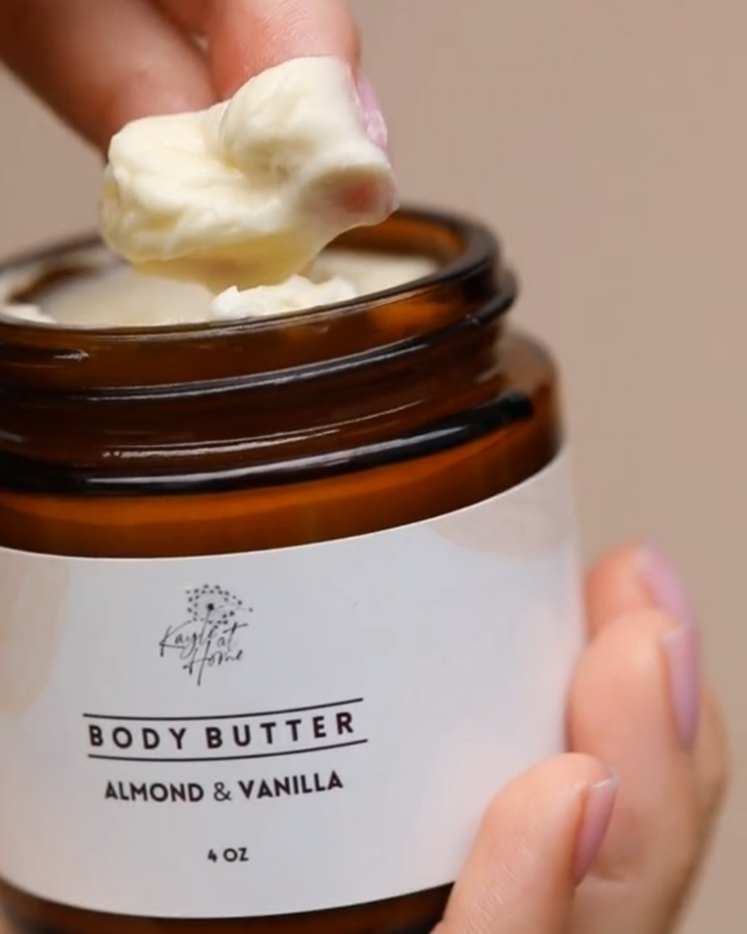 Close-up of fingers scooping creamy almond and vanilla body butter from glass jar